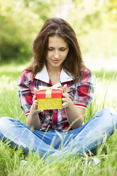 Vacker teen flicka med gåva i parken på grönt gräs. — Stockfoto