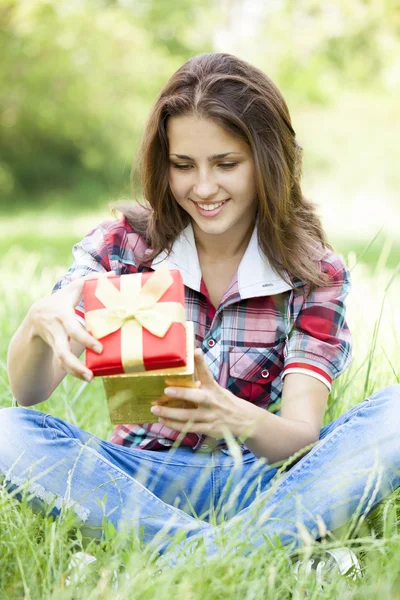 Красивая девушка-подросток с подарком в парке на зеленой траве . — стоковое фото