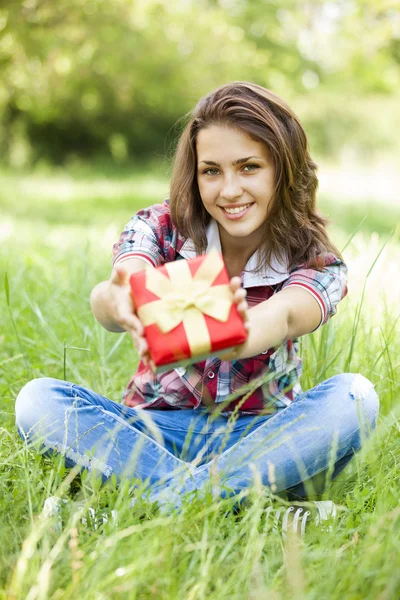 Красива дівчина-підліток з подарунком в парку на зеленій траві . — стокове фото