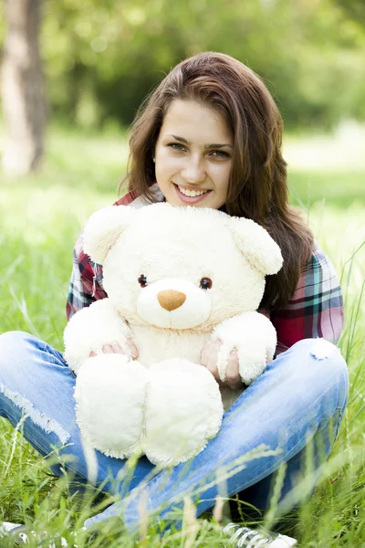 Красивая девушка-подросток с плюшевым мишкой в парке на зеленой траве . — стоковое фото