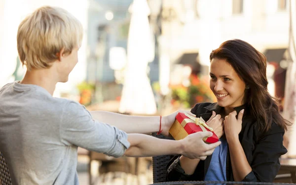 Ο νεαρός δίνει ένα δώρο σε ένα νεαρό κορίτσι στο καφέ. — Φωτογραφία Αρχείου