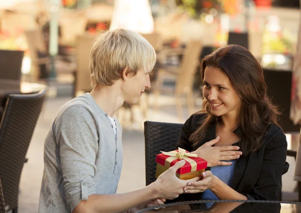De jongeman geeft een cadeau aan een jong meisje in het café. — Stockfoto