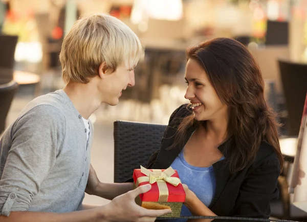 El joven le regala un regalo a una joven en el café. — Foto de Stock