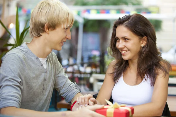The young man gives a gift to a young girl in the cafe — Stock Photo, Image
