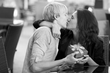 The young man gives a gift to a young girl in the cafe and they clipart