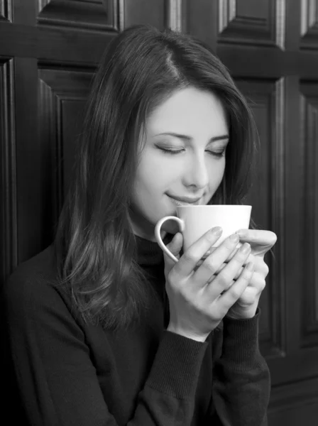 Chica de estilo bebiendo café cerca de puertas de madera. Foto en negro y con —  Fotos de Stock