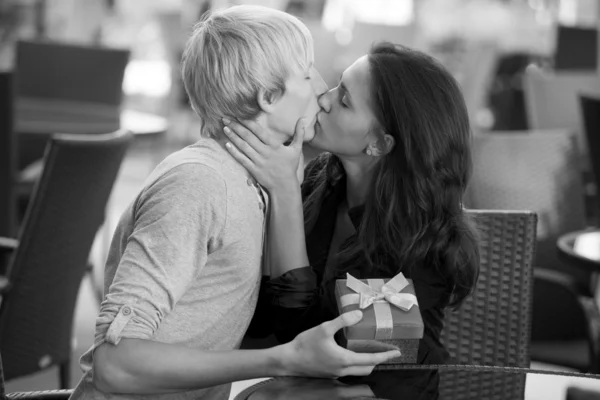 El joven le da un regalo a una joven en el café y ellos —  Fotos de Stock