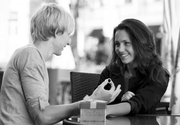 O jovem dá um presente para uma jovem no café — Fotografia de Stock