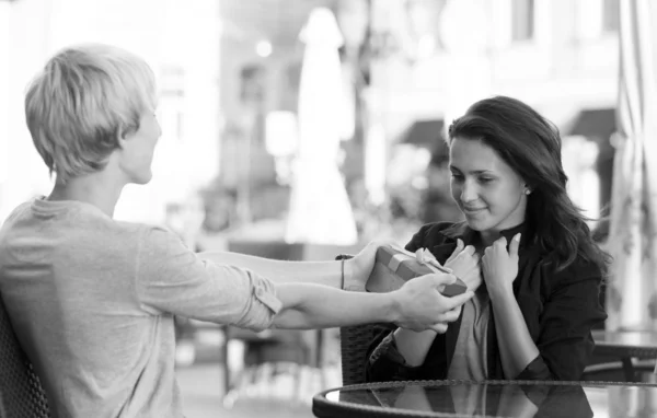 O jovem dá um presente para uma jovem no café — Fotografia de Stock