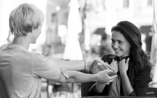 Der junge Mann beschenkt ein junges Mädchen im Café — Stockfoto
