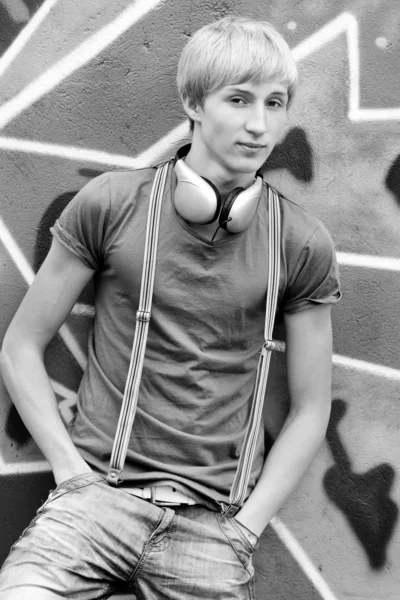 Stijl tiener jongen met koptelefoon in de buurt van graffiti achtergrond. — Stockfoto