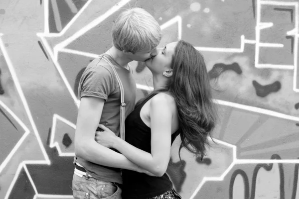 Młoda para całuje w pobliżu graffiti tło. — Zdjęcie stockowe