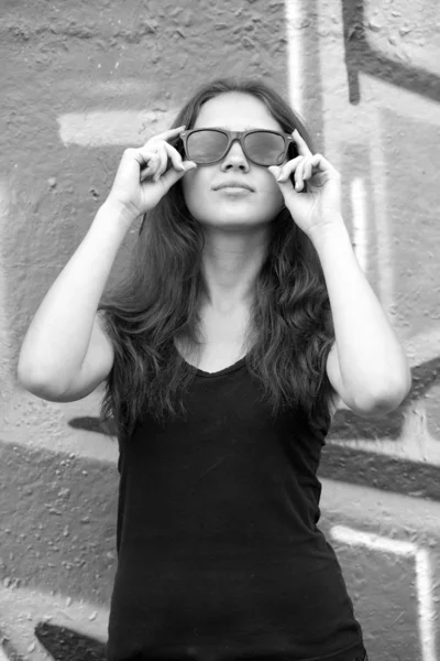 Stil tonåring flicka i solglasögon nära graffiti bakgrund. — Stockfoto