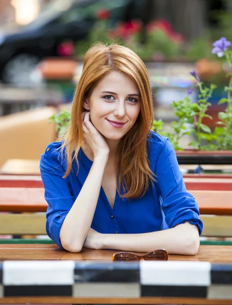 Стильная рыжая девушка сидит на скамейке в кафе — стоковое фото