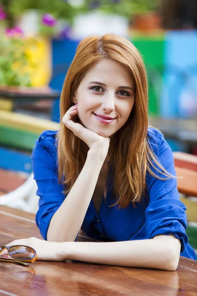 Стильная рыжая девушка сидит на скамейке в кафе — стоковое фото