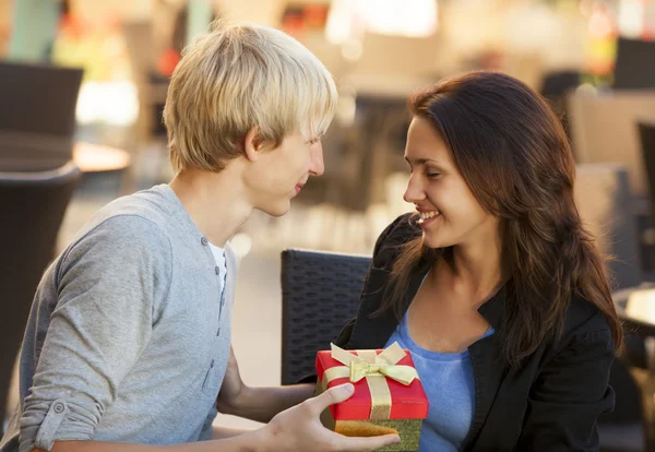 Den unge mannen ger en gåva till en ung flicka på caféet — Stockfoto