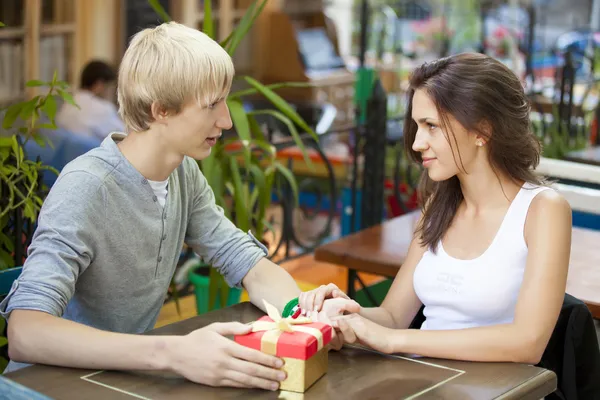 Ο νεαρός δίνει ένα δώρο σε ένα νεαρό κορίτσι στο καφέ. — Φωτογραφία Αρχείου