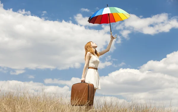Красивая рыжая девушка с зонтиком и чемоданом на открытом воздухе . — стоковое фото