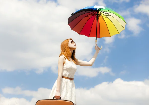 Hermosa chica pelirroja con paraguas y maleta en el cielo azul ba — Foto de Stock