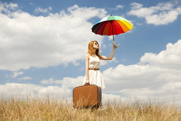 Hermosa chica pelirroja con paraguas y maleta al aire libre . — Foto de Stock