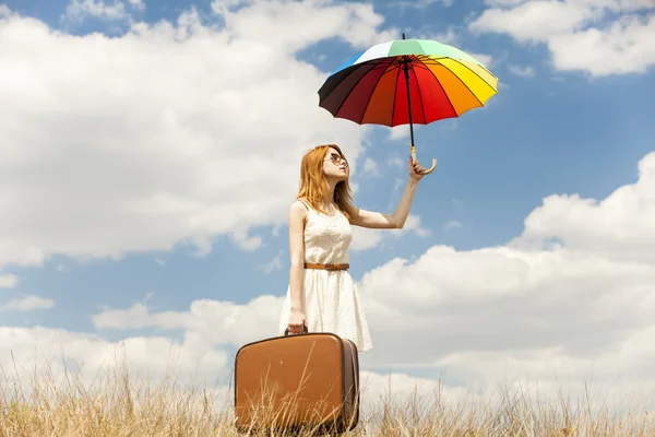 Krásná rusovláska dívka s deštníkem a kufr na venkovní. — Stock fotografie