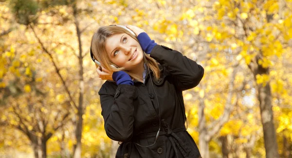 Flicka med hörlurar på hösten park. — Stockfoto