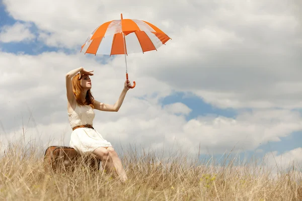 Hermosa chica pelirroja con paraguas y maleta al aire libre . — Foto de Stock