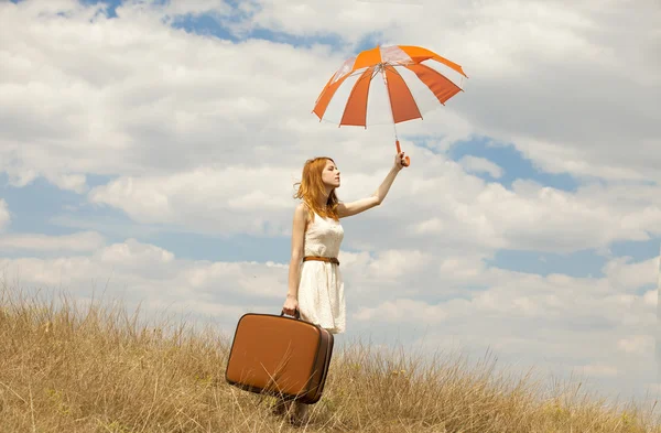 Красивая рыжая девушка с зонтиком и чемоданом на открытом воздухе . — стоковое фото