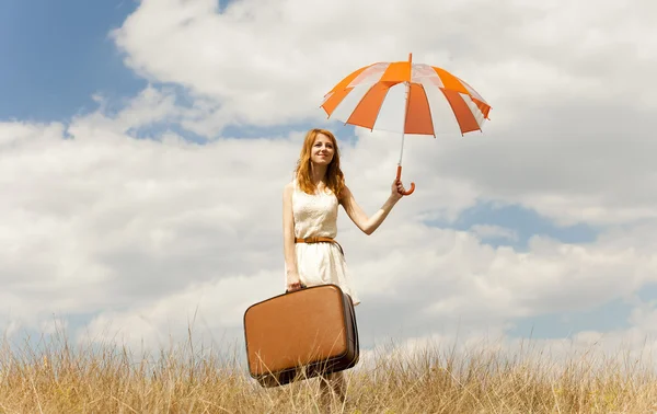 Bella ragazza rossa con ombrello e valigia all'aperto . — Foto Stock