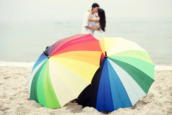 Par kyssar på stranden och paraply — Stockfoto