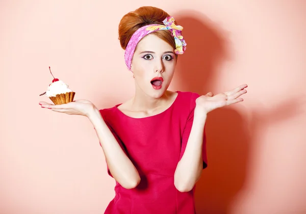 Stijl roodharige meisje met cake bij roze achtergrond. — Stockfoto