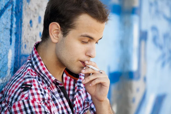 Jonge tiener jongen roken in de buurt van graffiti muur. — Stockfoto