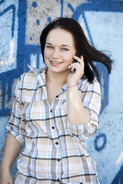 Tiener meisje stijl bellen via de telefoon in de buurt van graffiti achtergrond. — Stockfoto