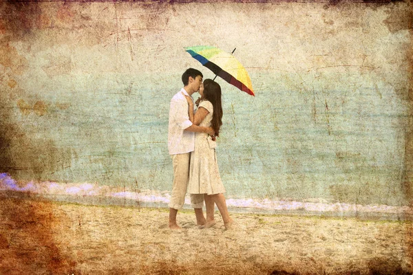 Couple kissing under umbrella at the beach — Stock Photo, Image