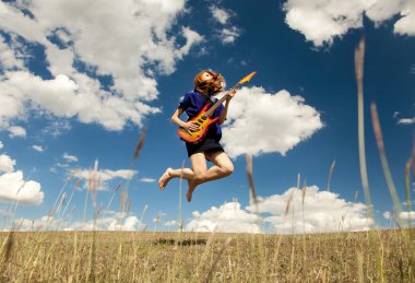 Redhead girl jumping with guitar at outdoor.