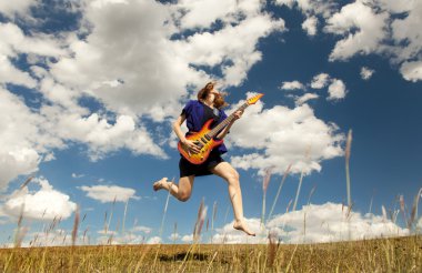 Redhead girl jumping with guitar at outdoor.