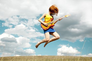 Redhead girl jumping with guitar at outdoor.