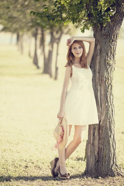 Roodharige meisje met hoed in de buurt van boom. — Stockfoto