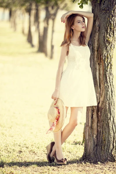 Roodharige meisje met hoed in de buurt van boom. — Stockfoto