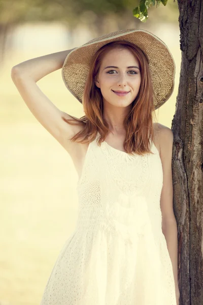 Κοκκινομάλλα κοπέλα με καπέλο κοντά δέντρο. — Φωτογραφία Αρχείου