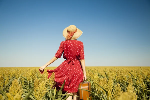 Rödhårig tjej med resväska på sädesfält. — Stockfoto