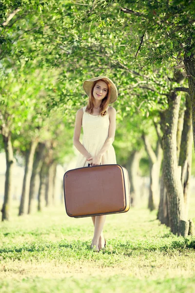 Rusovláska dívka s kufrem v stromu alley. — Stock fotografie
