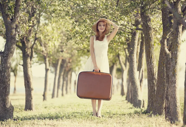 Redhead girl with suitcase at tree's alley. — Stock Photo, Image