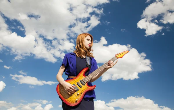Рыжая девушка с гитарой на фоне неба . — стоковое фото