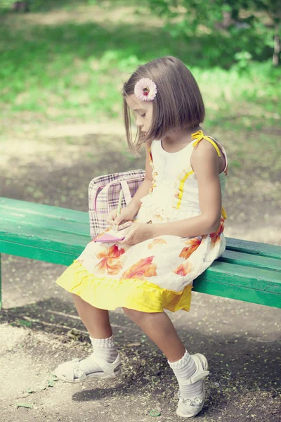 Criança senta-se no banco no parque . — Fotografia de Stock