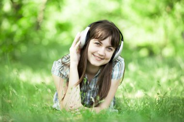 Yeşil bahar çimlerinde kulaklıklı genç bir moda kızı..