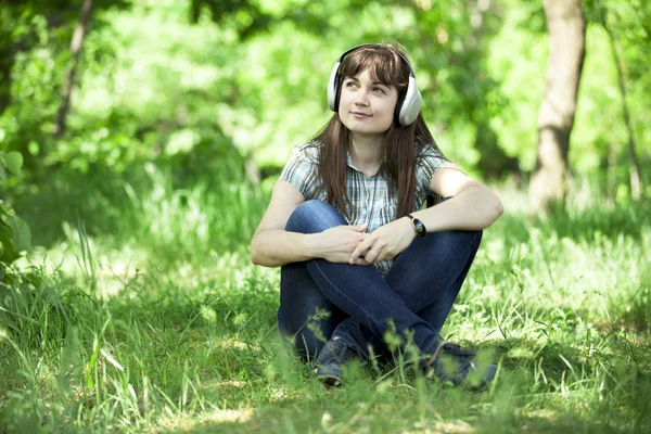 Yeşil bahar çimlerinde kulaklıklı genç bir moda kızı.. — Stok fotoğraf