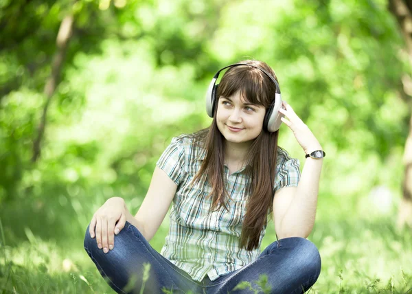 Yeşil bahar çimlerinde kulaklıklı genç bir moda kızı.. — Stok fotoğraf