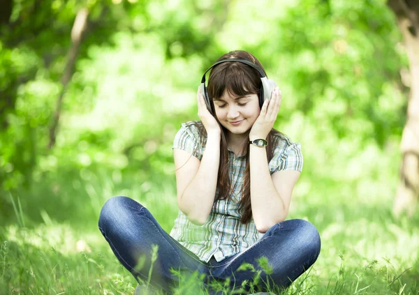 Menina de moda jovem com fones de ouvido na grama de primavera verde . — Fotografia de Stock