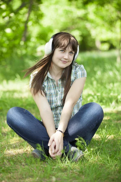 Mladá módní dívka se sluchátky na zelené jarní trávě. — Stock fotografie